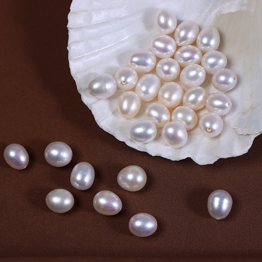 Loose half-drilled pearls displayed on a brown fabric and white shell, showcasing slight pink and ivory tones.