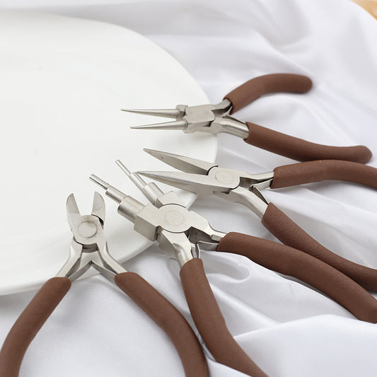 Flat lay of all 4 brown handle jewelry pliers on a white fabric background.