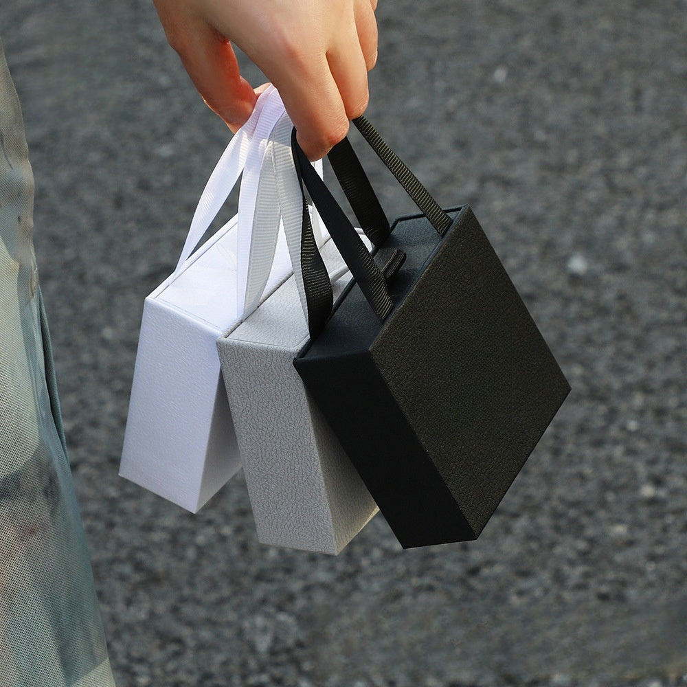 Jewelry drawer gift boxes in white, grey, and black being held in hand